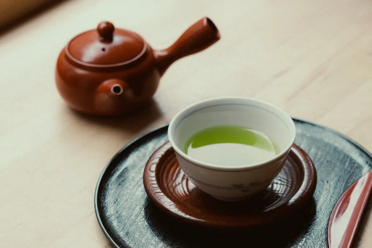 A handleless Japanese cup of pale green sencha beside a small side-handled teapot