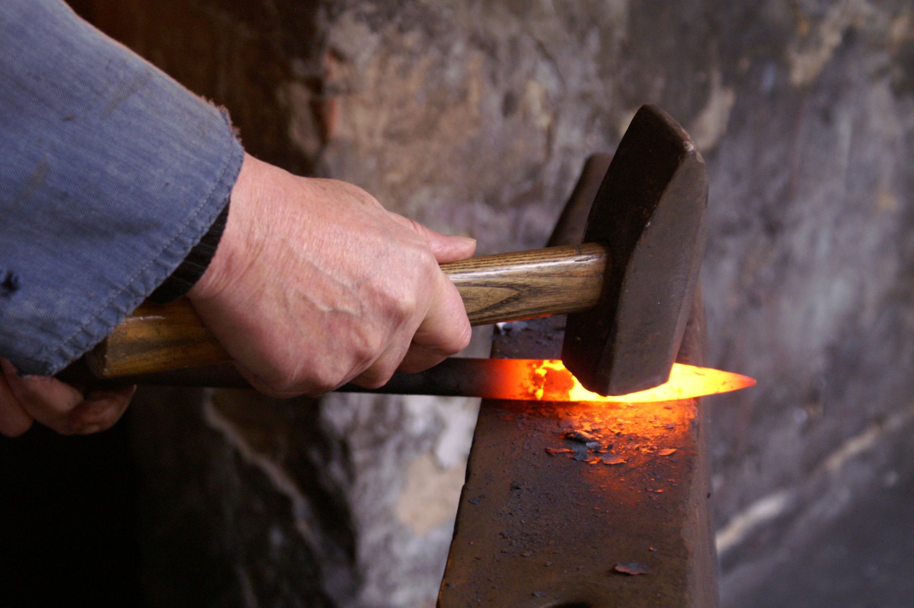 Blacksmith hammering red-hot steel on anvil in traditional Japanese knife forge with charcoal fire glowing.