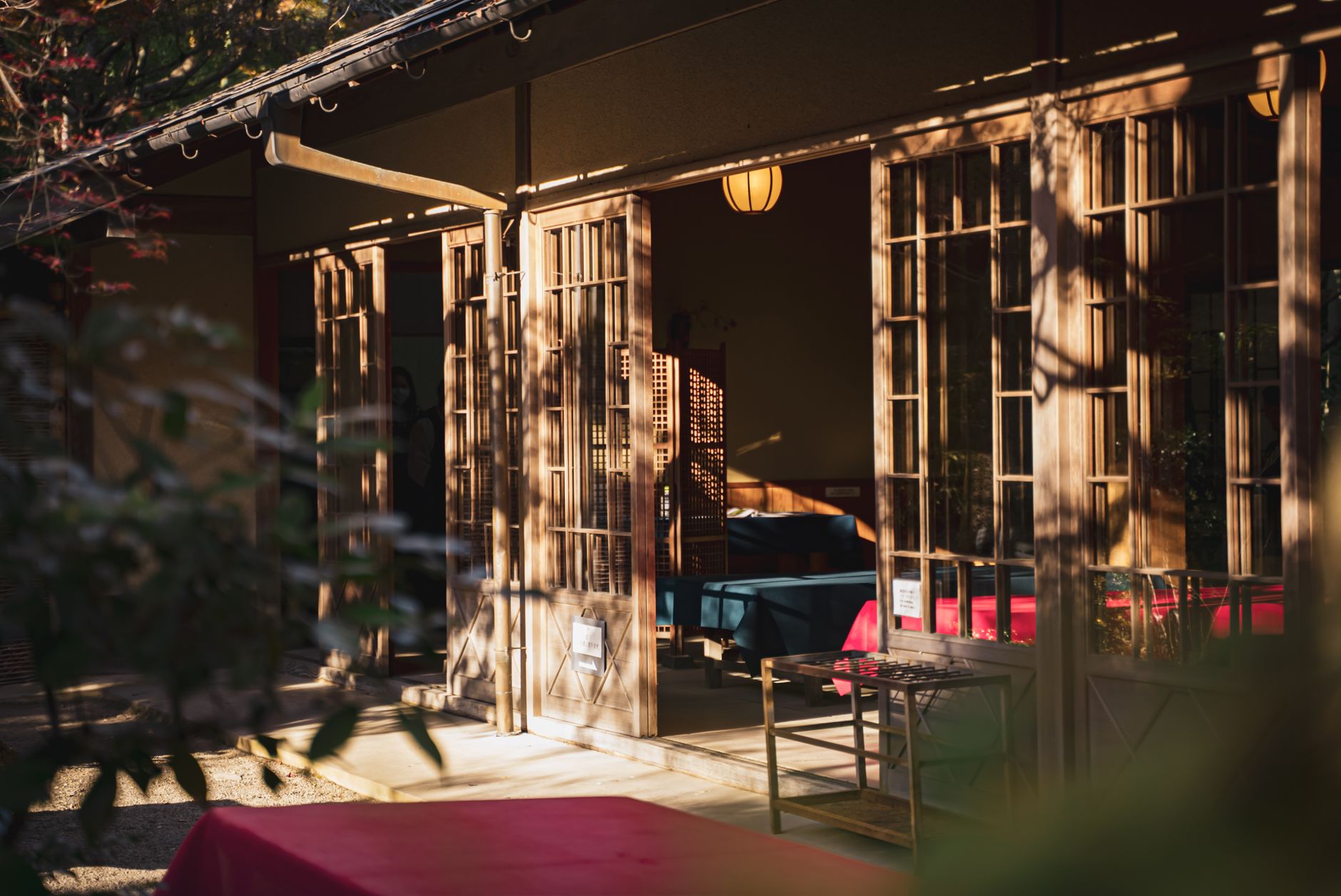 Traditional Japanese tea room showing low ceiling with exposed wooden beams, tatami flooring, tokonoma alcove, and small square window casting natural light.
