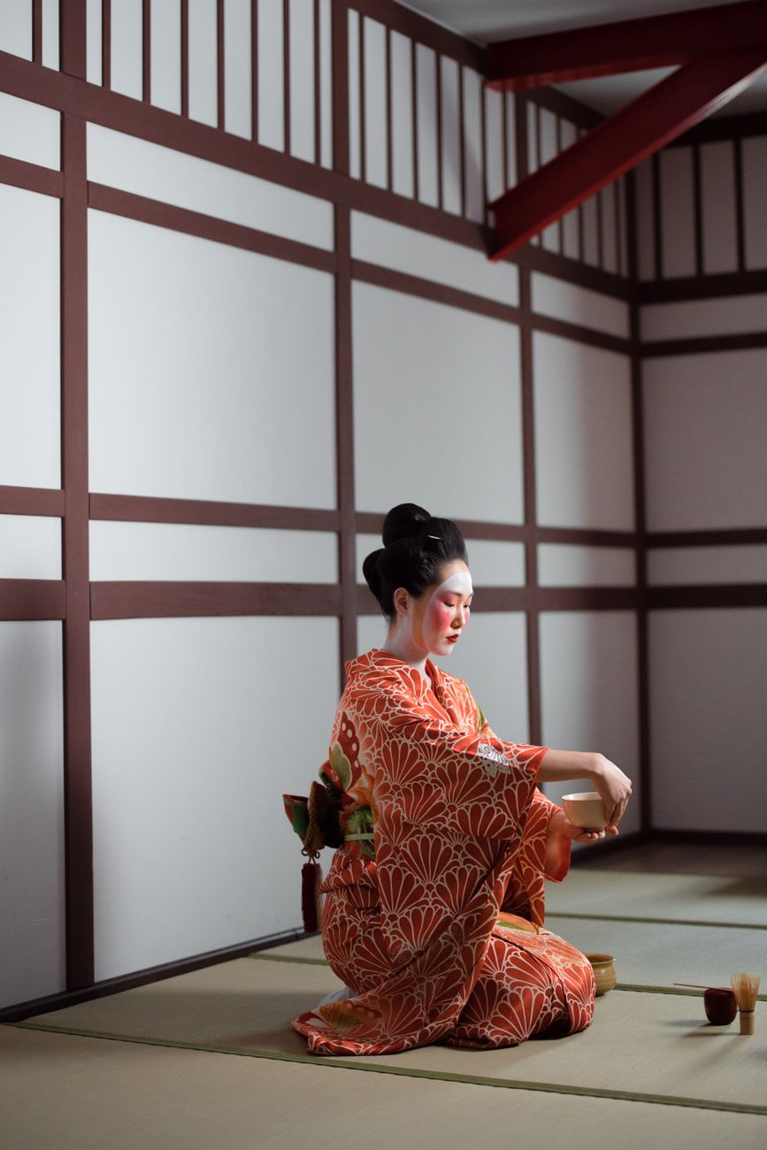 Traditional Japanese tea room showing low ceiling with exposed wooden beams, tatami flooring, tokonoma alcove, and small square window casting natural light.
