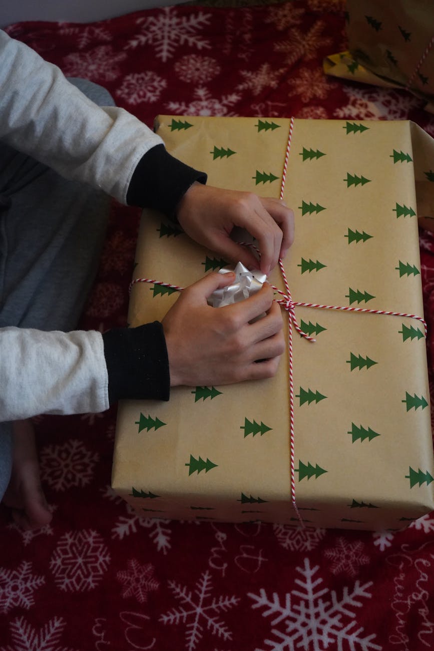 Hands carefully folding decorative washi paper around a small box with precise creases and traditional mizuhiki cord arrangement.