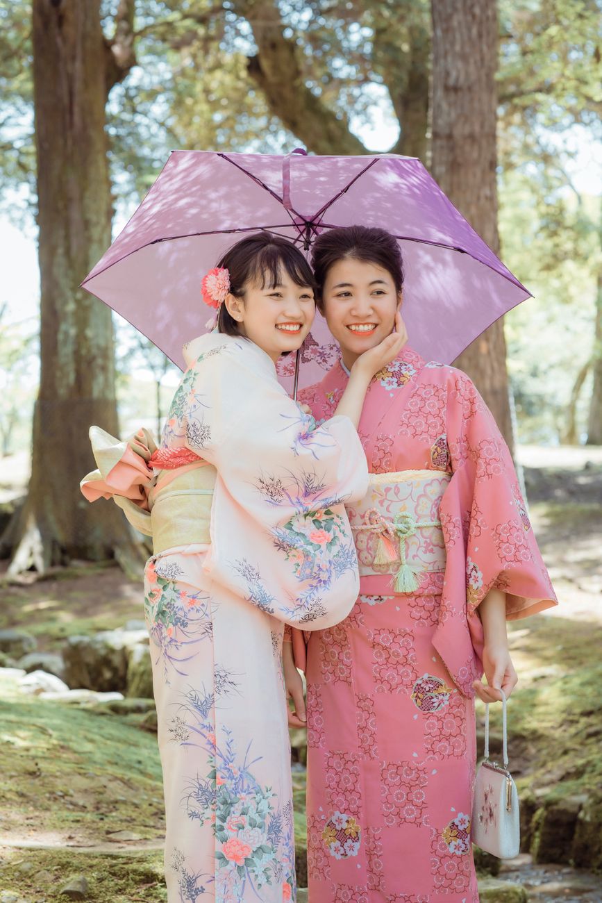 Two hands presenting a wrapped gift with both palms in traditional Japanese manner, cloth furoshiki wrapping visible.