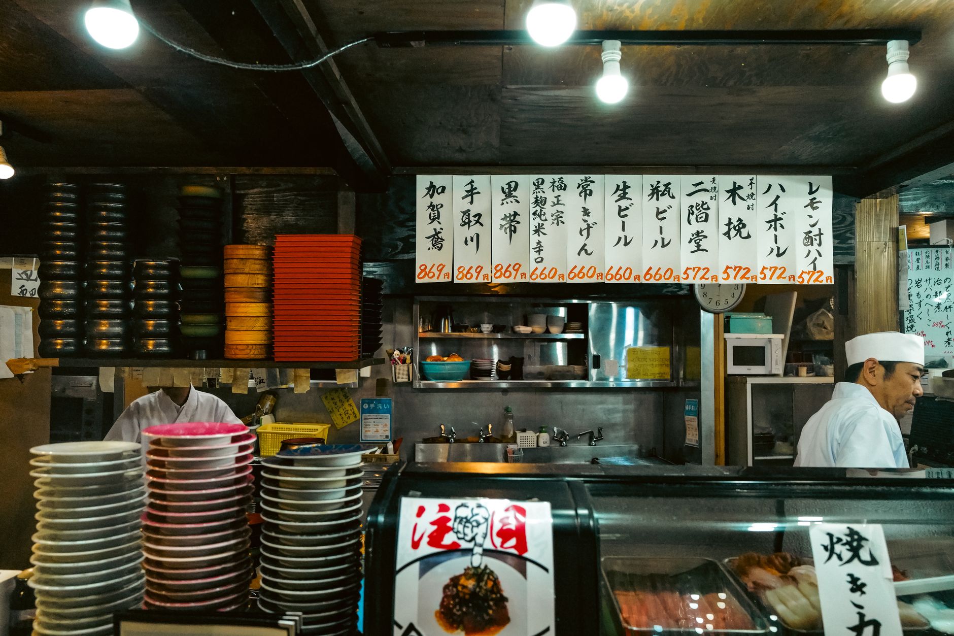 Hands holding chopsticks over a traditional Japanese meal with rice bowl, miso soup, and small side dishes on lacquerware.