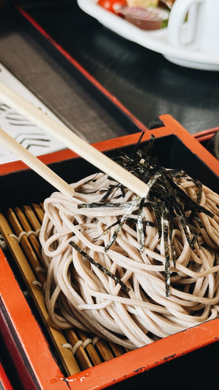 Hands holding chopsticks over a traditional Japanese meal with rice bowl, miso soup, and small side dishes on lacquerware.
