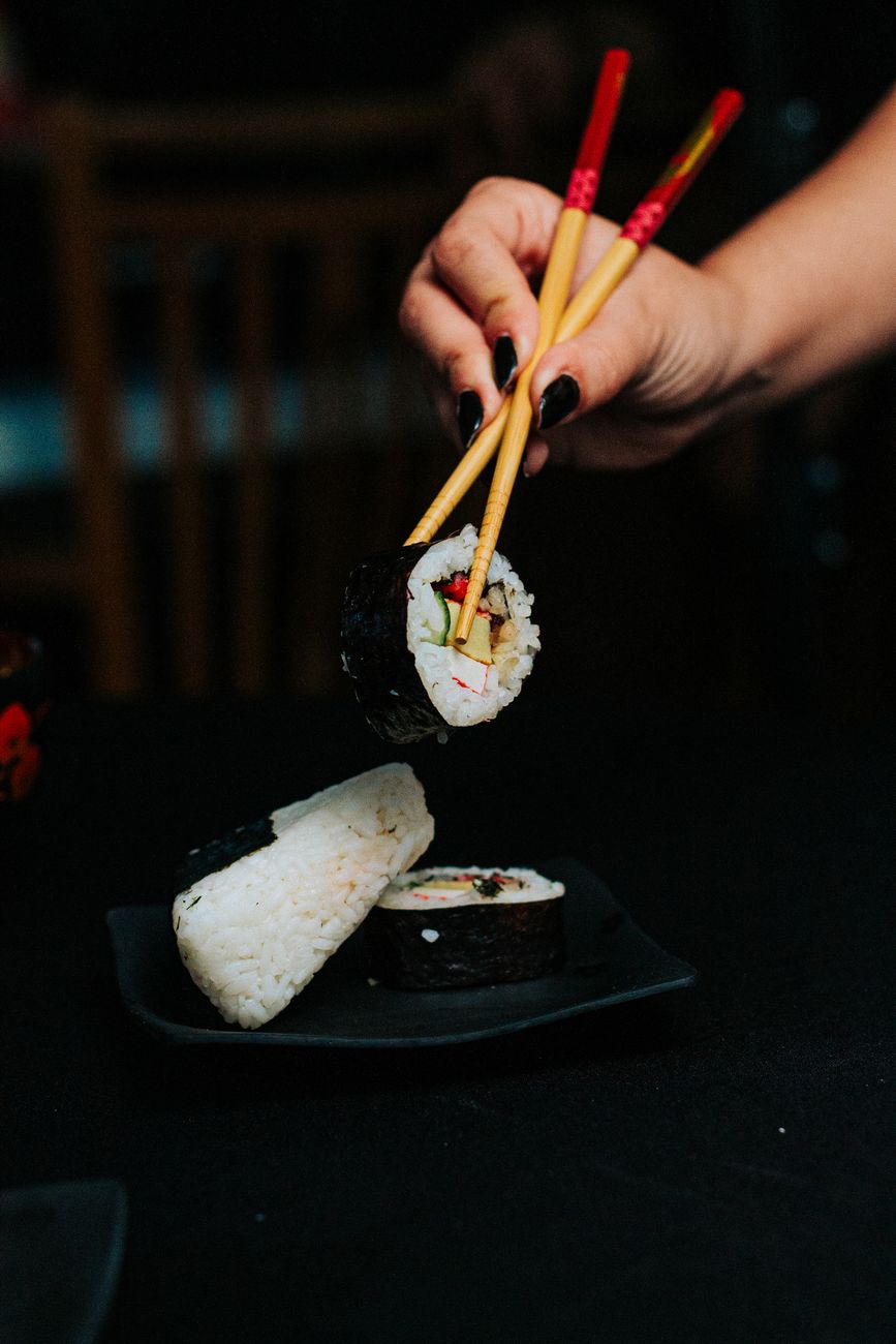 Hands holding chopsticks incorrectly positioned vertically in a bowl of white rice at a traditional Japanese table setting.
