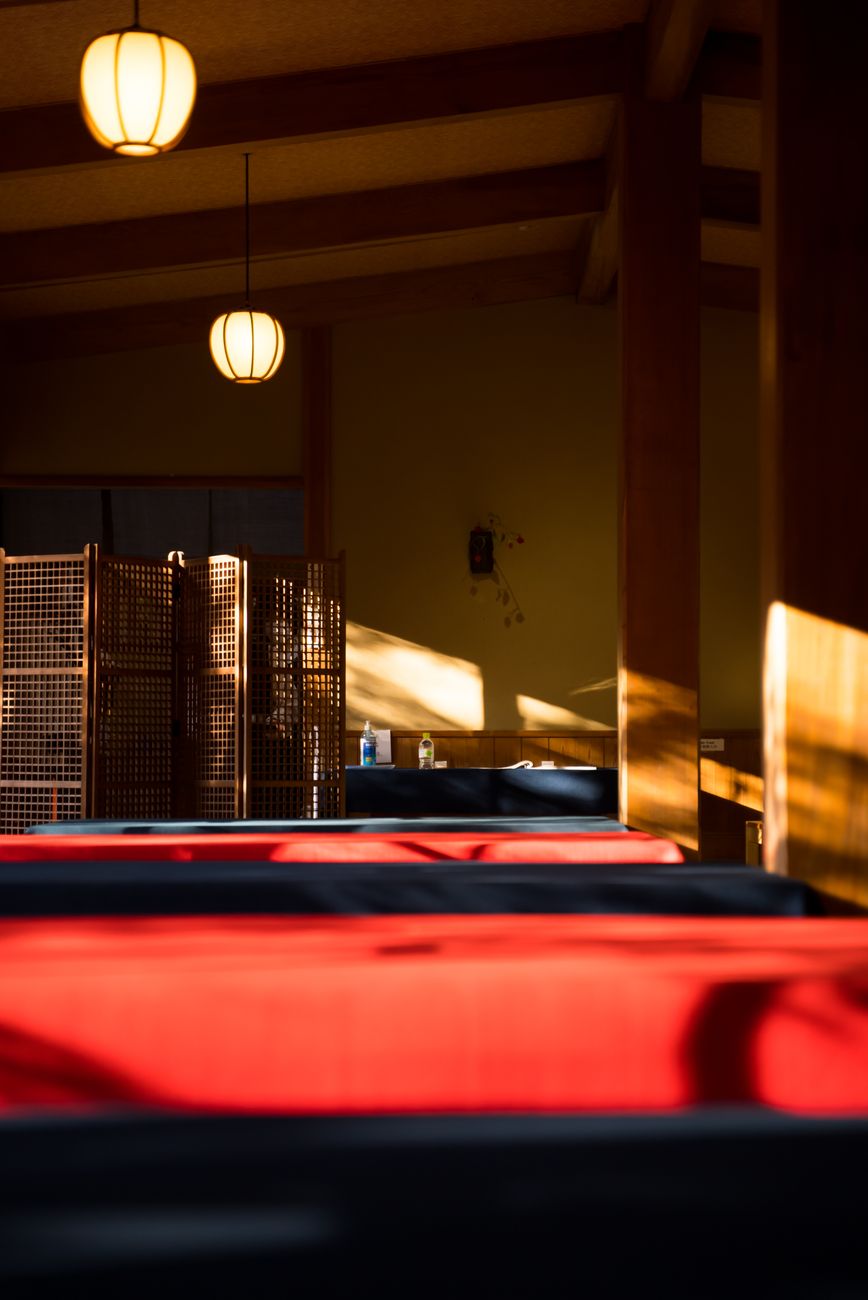 Guests in yukata robes walking along a traditional wooden corridor toward an outdoor onsen bath at sunset.
