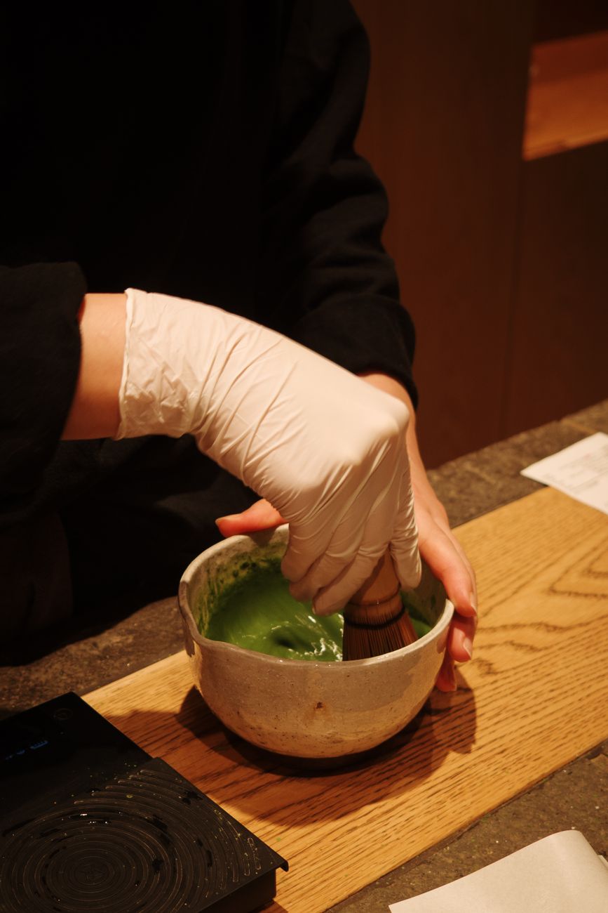 Person in kimono lifting a ceramic tea bowl to their lips during a traditional Japanese tea ceremony