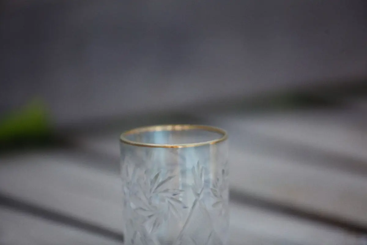 Artisan cutting intricate geometric patterns into clear glass tumbler using rotating grinding wheel in traditional Tokyo workshop.