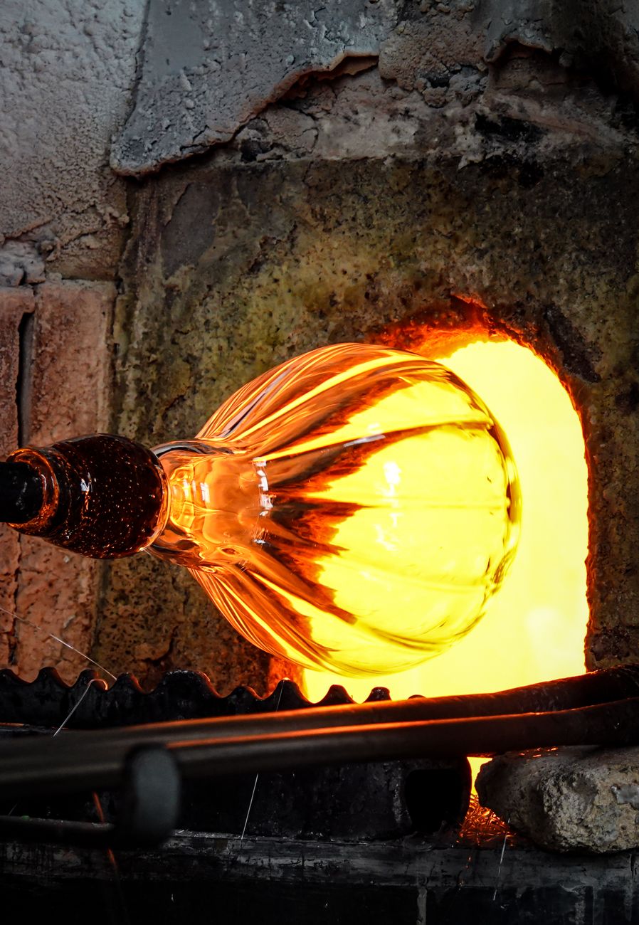 Artisan gathering molten Tsugaru Bidoro glass on a blowpipe from a furnace glowing with intense orange heat.