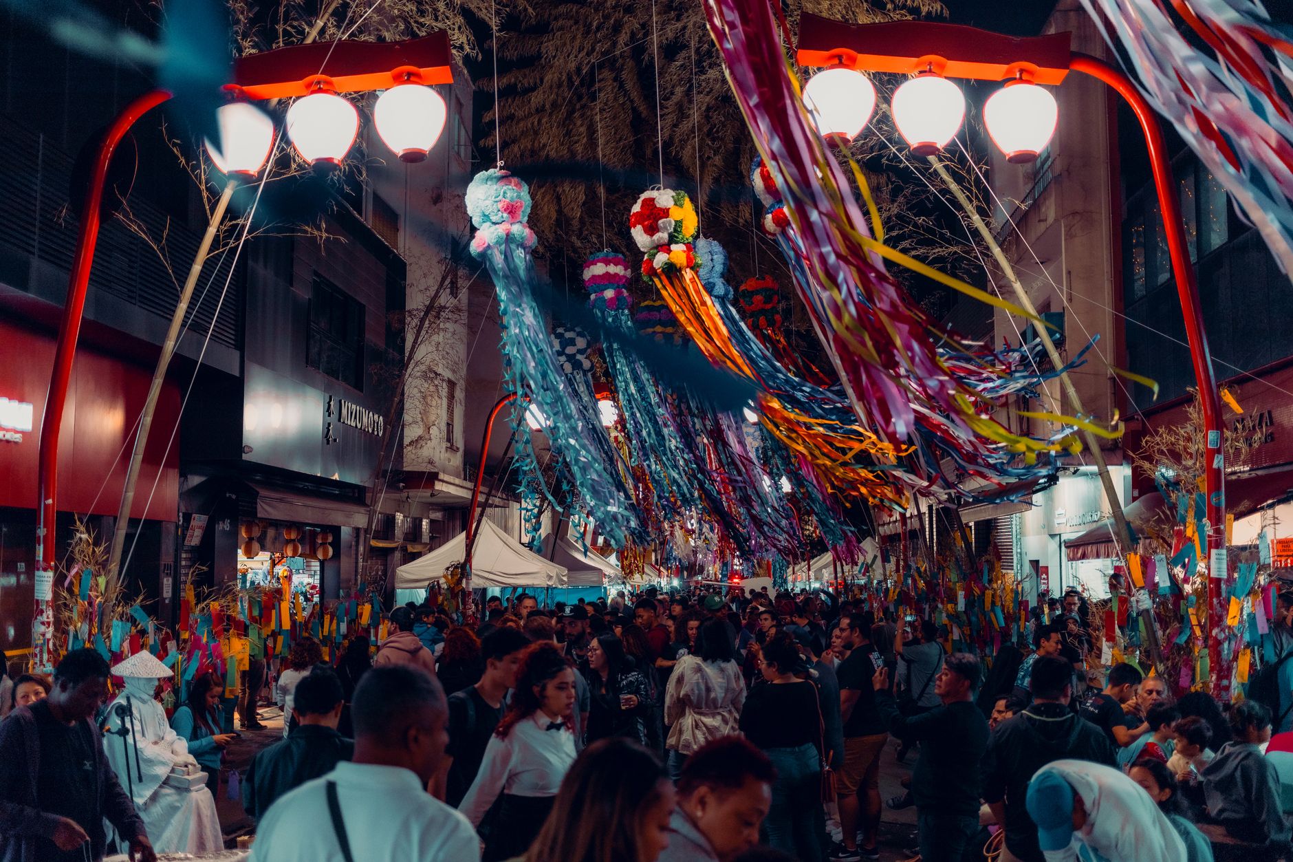 Families gather at a Buddhist temple during Obon, placing lit lanterns near ancestral graves decorated with fresh flowers.