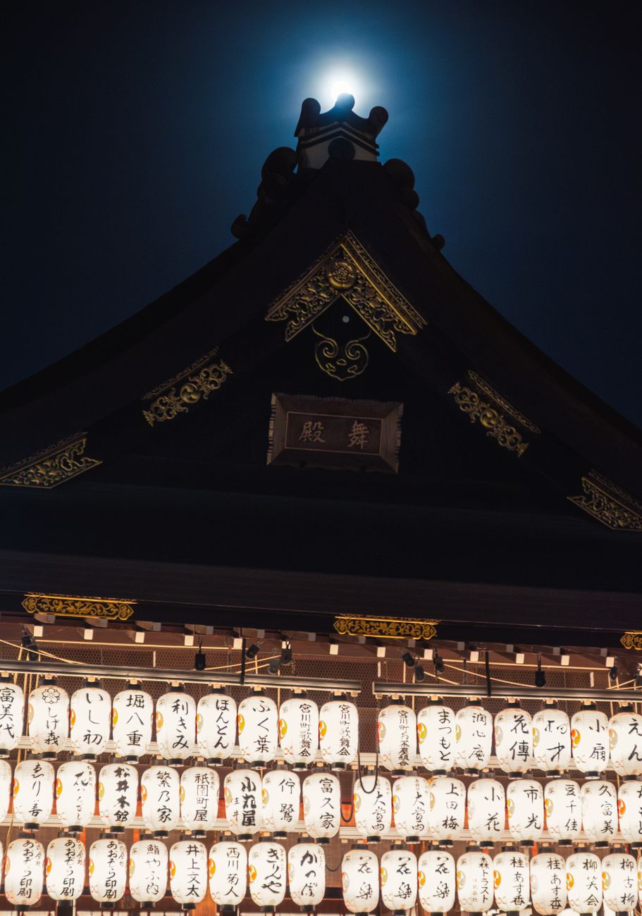 Families gather at a Buddhist temple during Obon, placing lit lanterns near ancestral graves decorated with fresh flowers.