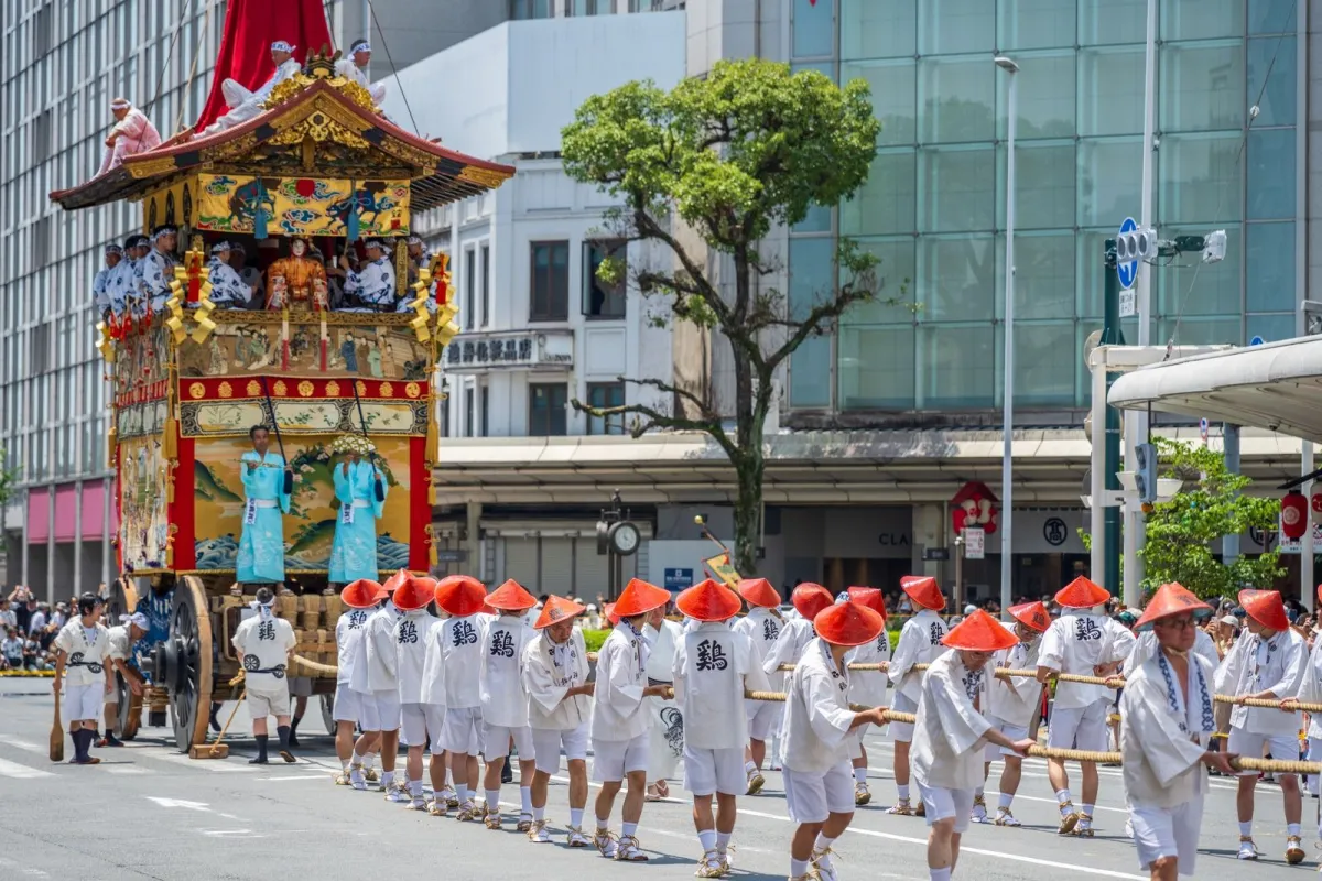 A towering wooden Gion Matsuri float decorated with tapestries moving through a Kyoto street