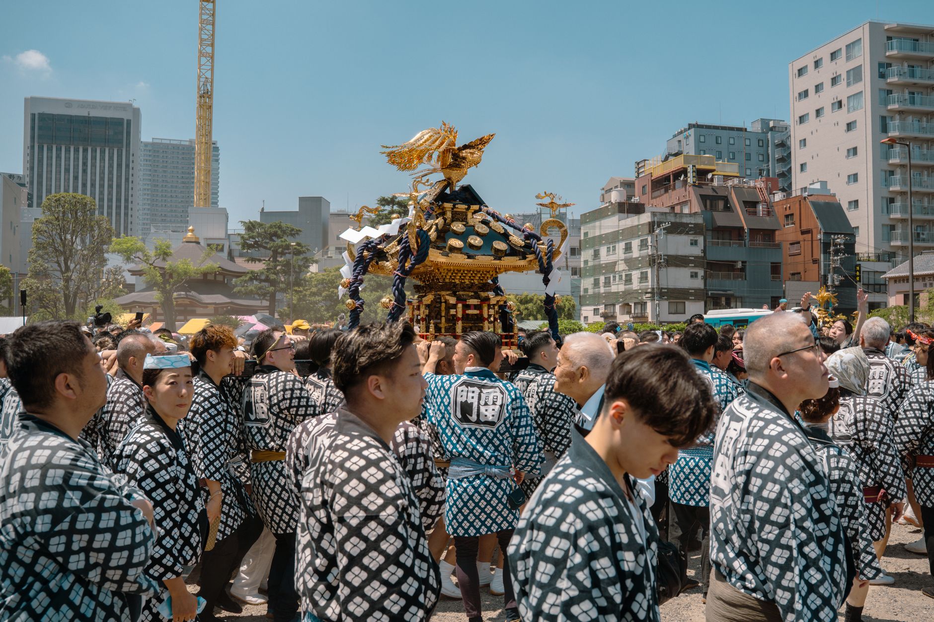 Local festival participants in traditional happi coats carry an ornate golden mikoshi portable shrine through a crowded Japanese street during summer matsuri.