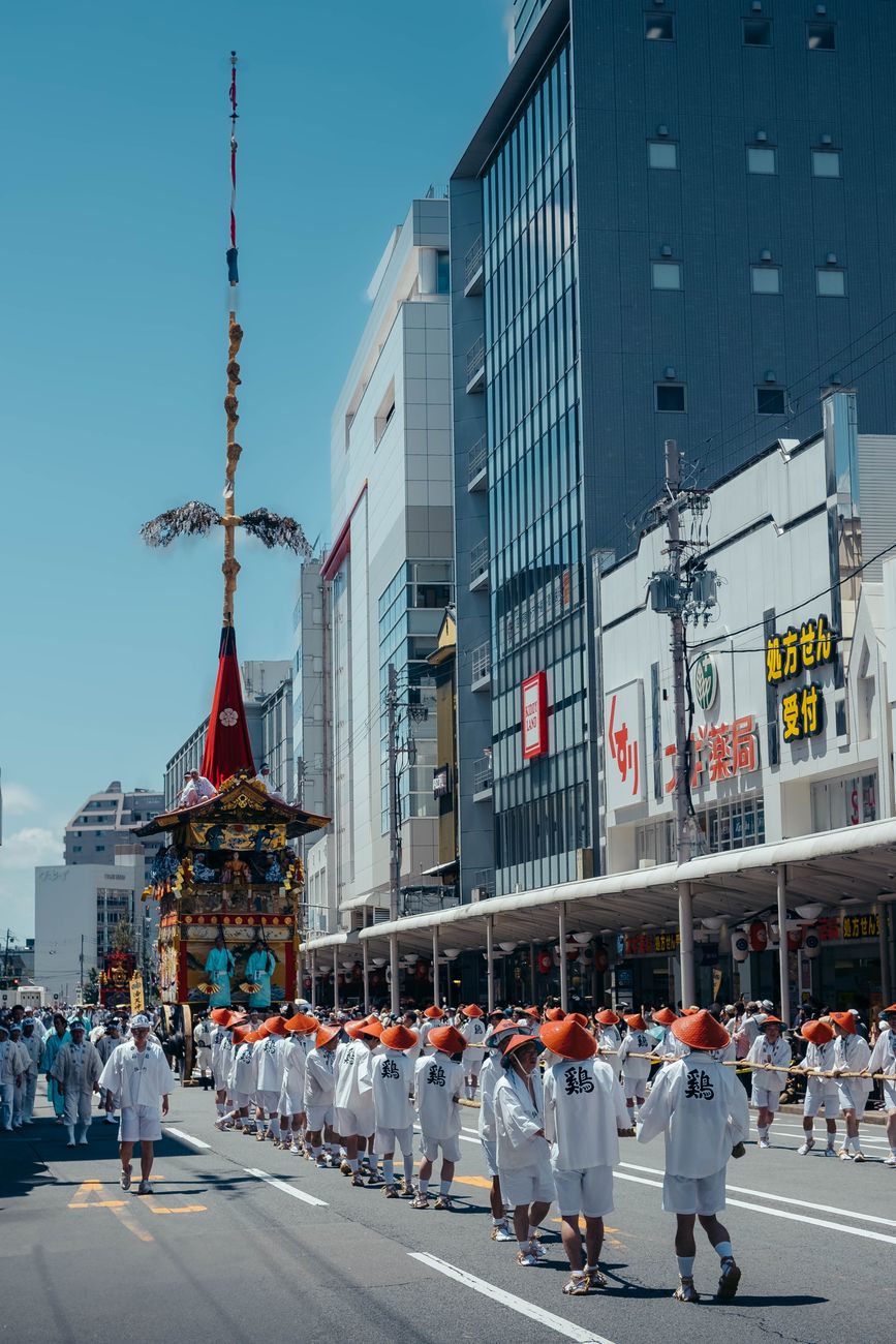 Local festival participants in traditional happi coats carry an ornate golden mikoshi portable shrine through a crowded Japanese street during summer matsuri.