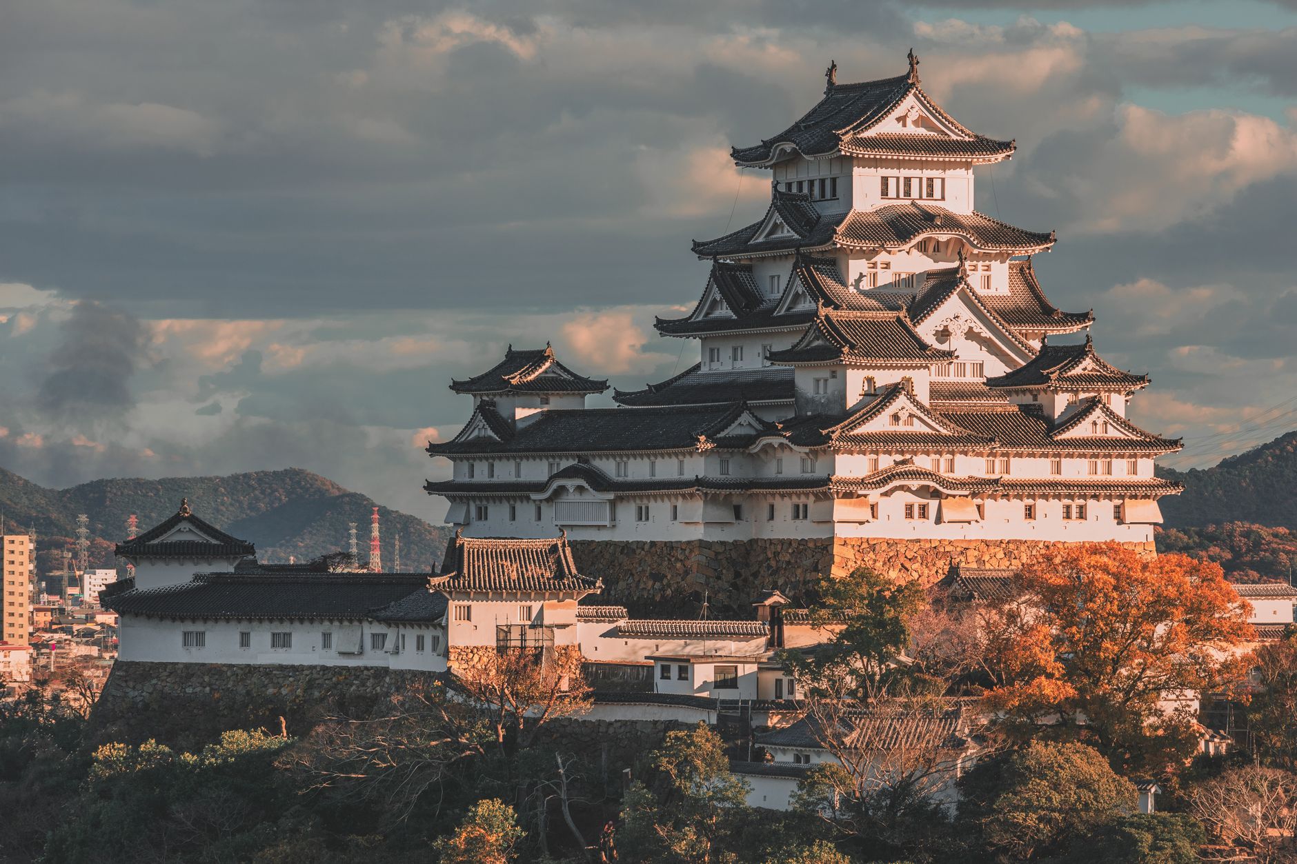 Massive curved stone walls rise in precise tiers beneath a multi-story wooden castle tower with white plaster and dark timber.