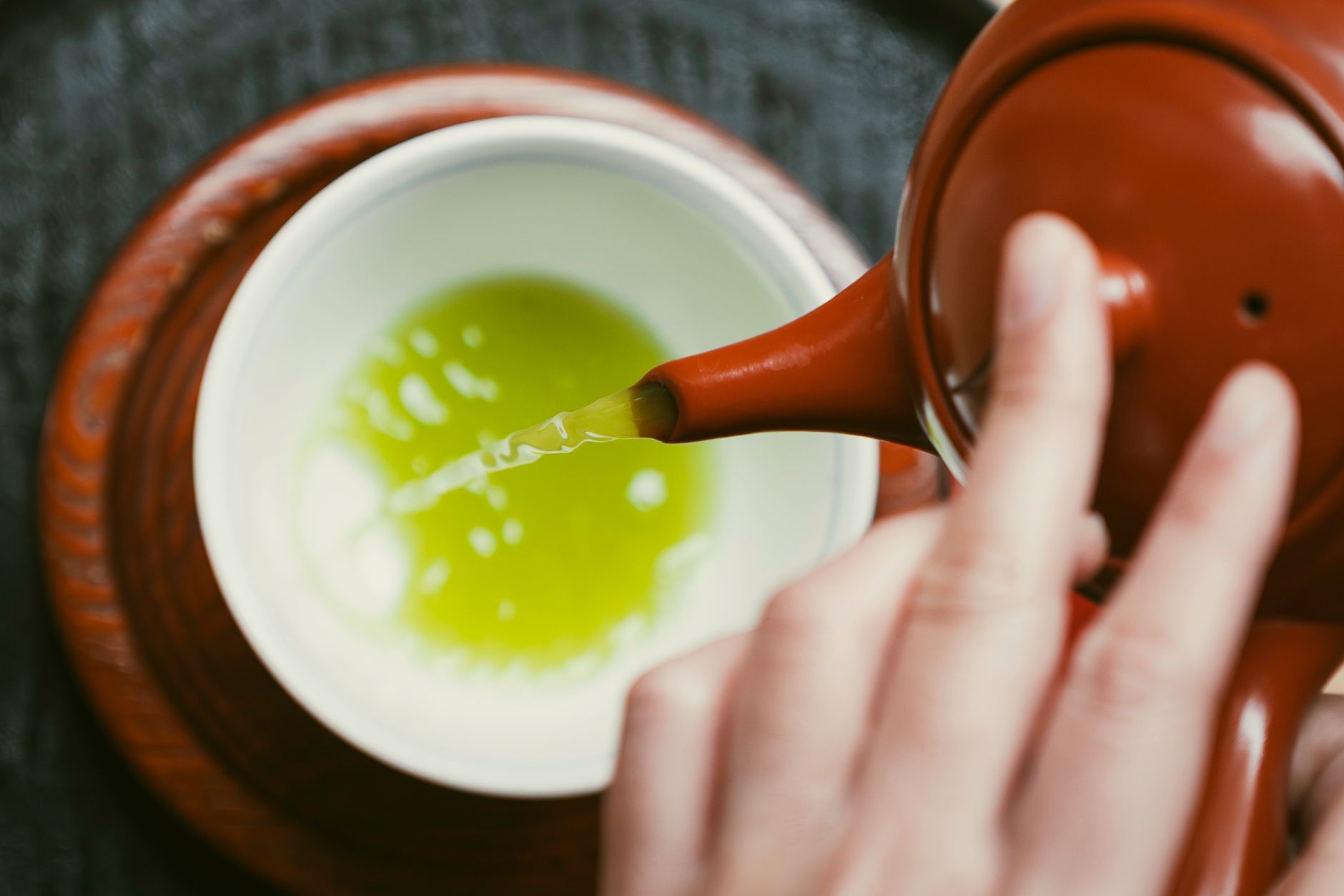 Vibrant green matcha powder in a ceramic bowl beside fresh sencha tea leaves on a bamboo mat.
