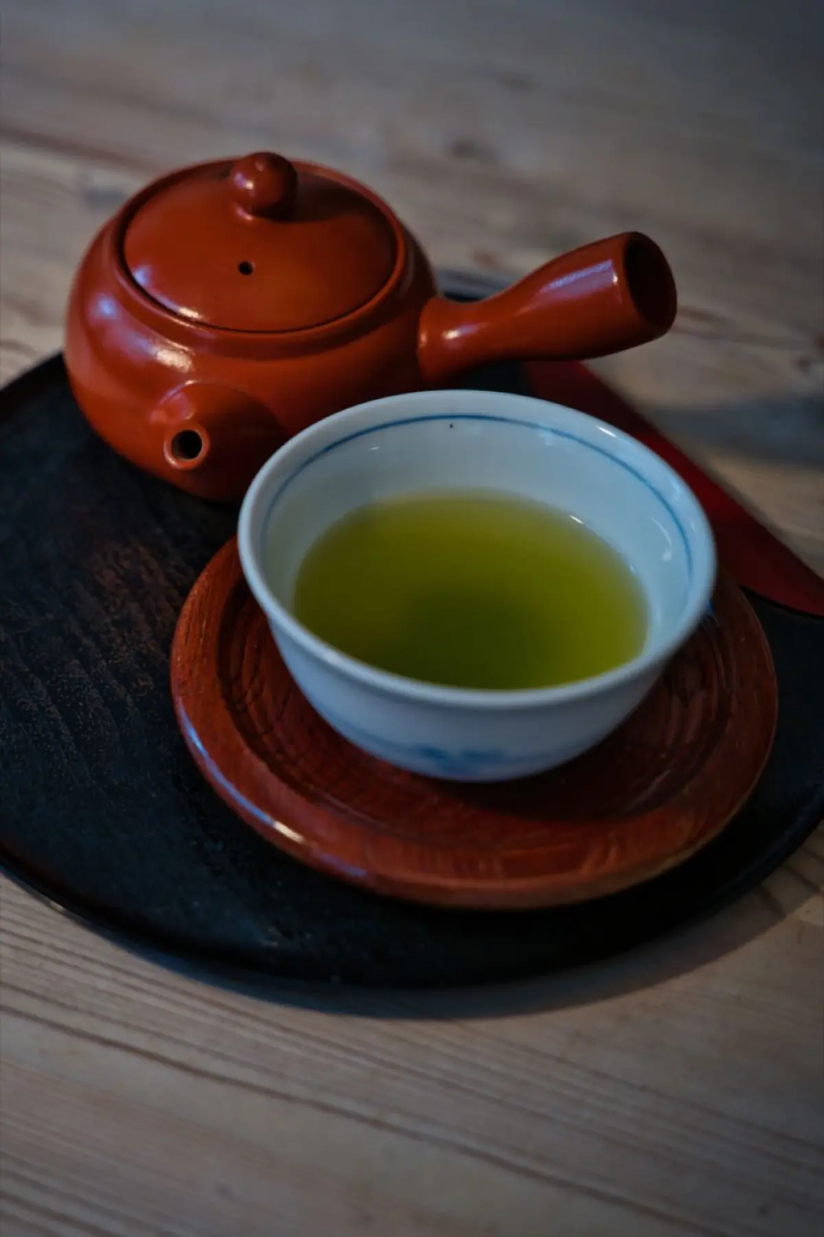 Vibrant green matcha powder in a ceramic bowl beside fresh sencha tea leaves on a bamboo mat.