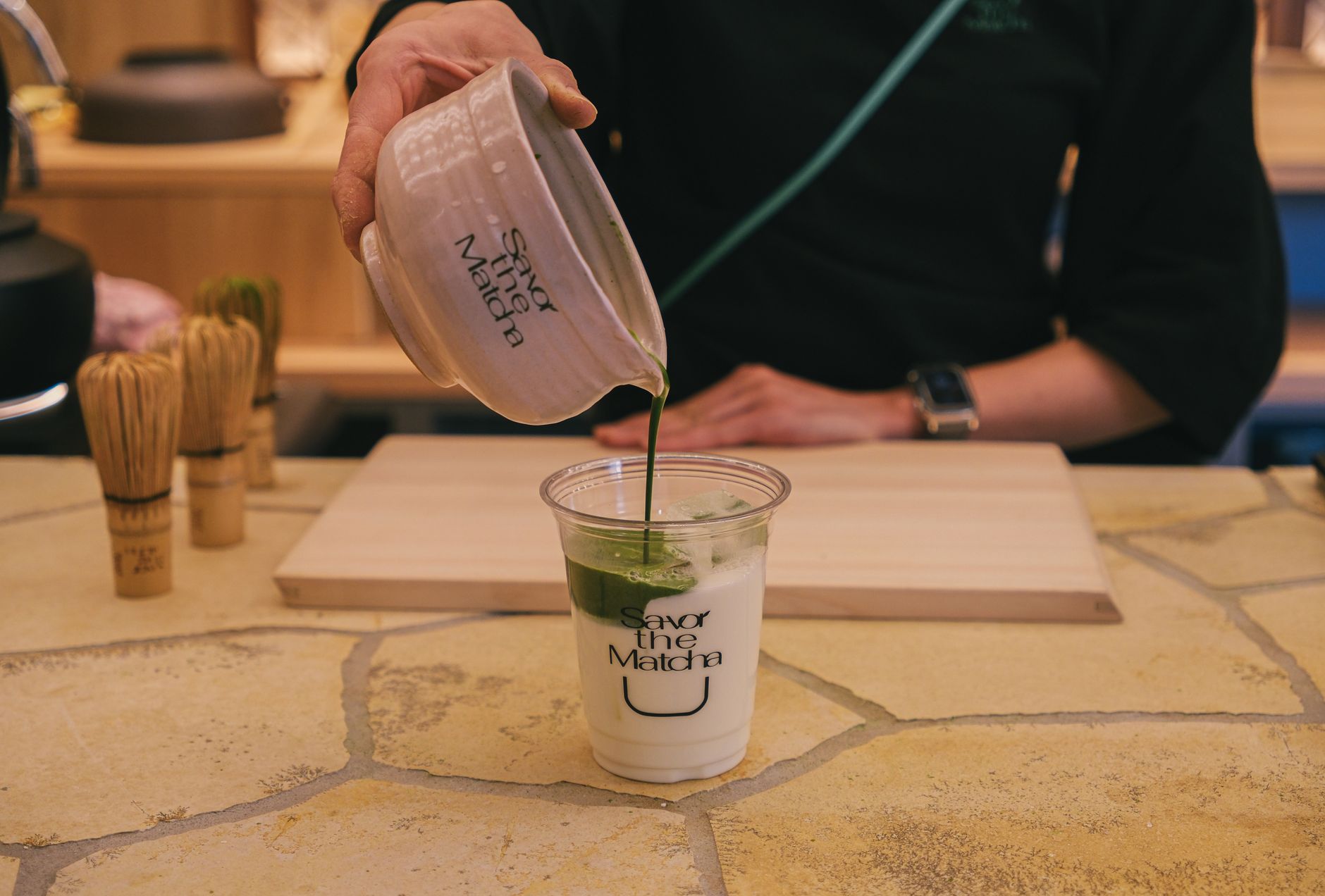 Traditional granite millstone grinding vibrant green tea leaves into fine matcha powder in a Japanese tea production facility.