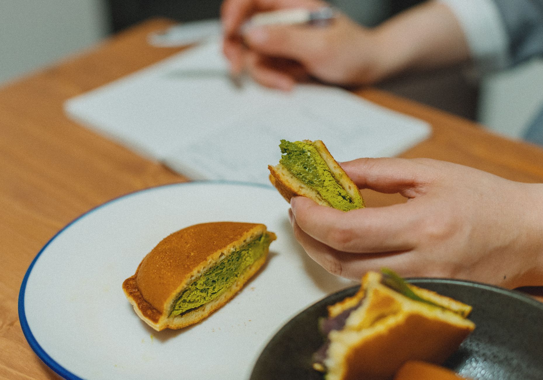 Vibrant green matcha powder in a ceramic bowl beside bamboo whisk in traditional Nishio tea garden setting.