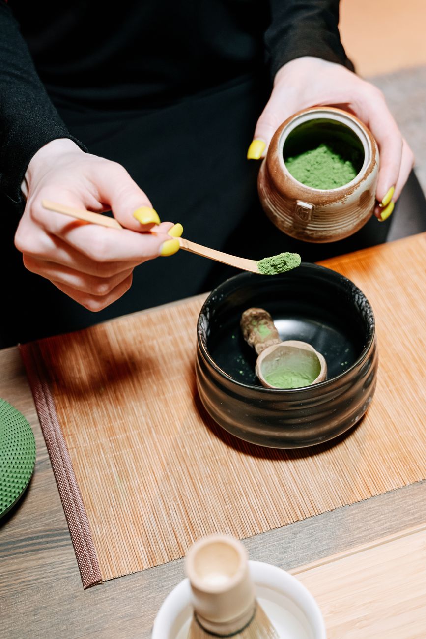 Traditional stone mill grinding vibrant green matcha powder in a Japanese tea ceremony room with bamboo utensils nearby.