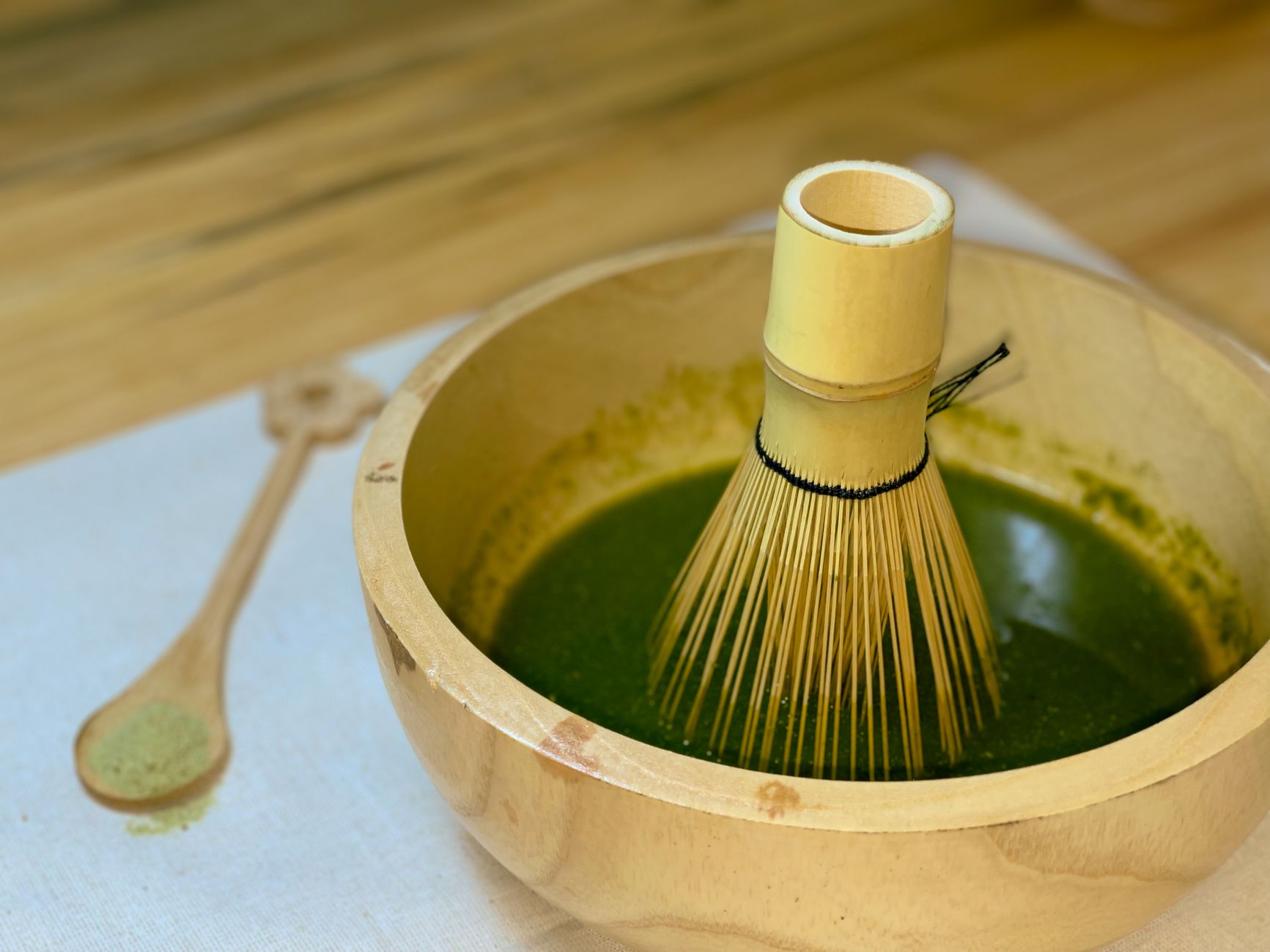 Traditional Japanese tea ceremony host whisking vibrant green matcha powder in a black ceramic bowl using bamboo whisk.