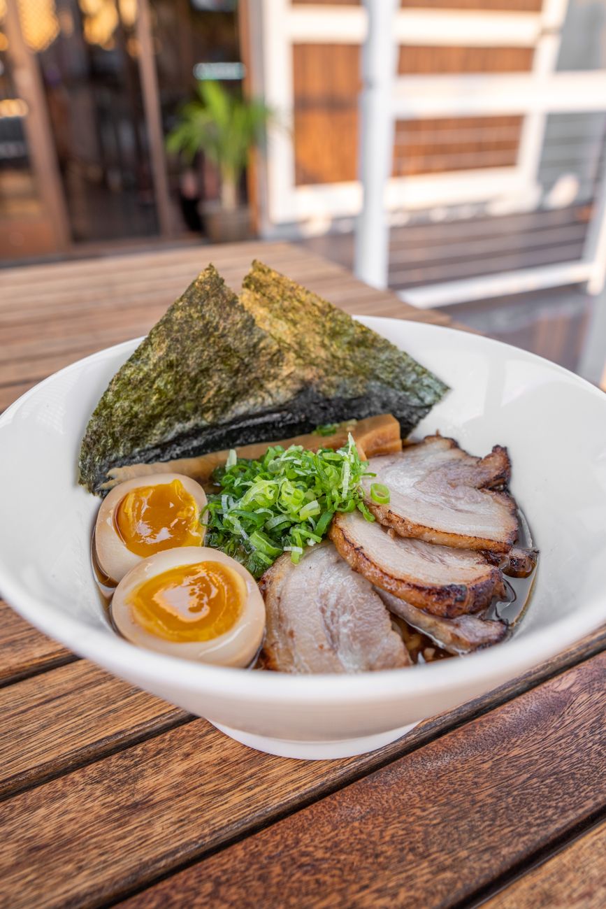 Hands straining kombu kelp and katsuobushi bonito flakes from steaming water in a traditional Japanese kitchen pot.