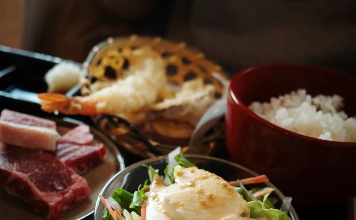 Traditional Japanese meal arrangement showing miso soup, pickled vegetables, grilled fish, rice, and soy sauce demonstrating five flavor elements