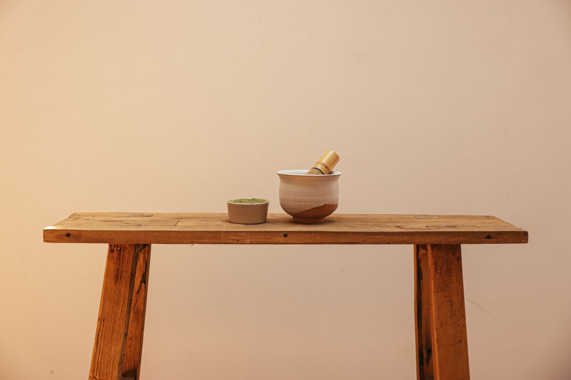 Traditional Japanese chasen bamboo whisk with fine prongs resting beside a bowl of bright green matcha powder.