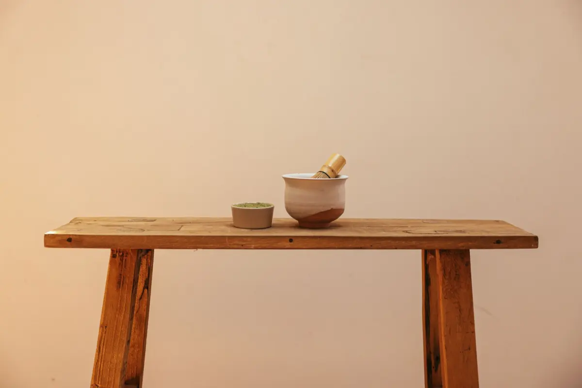 Traditional Japanese chasen bamboo whisk with fine prongs resting beside a bowl of bright green matcha powder.