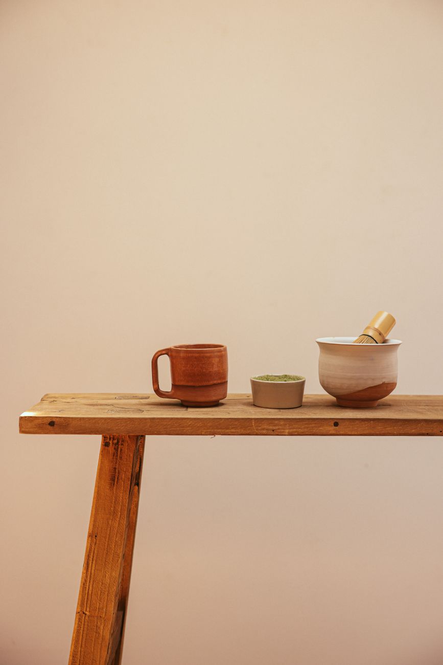 Traditional Japanese chasen bamboo whisk with fine prongs resting beside a bowl of bright green matcha powder.