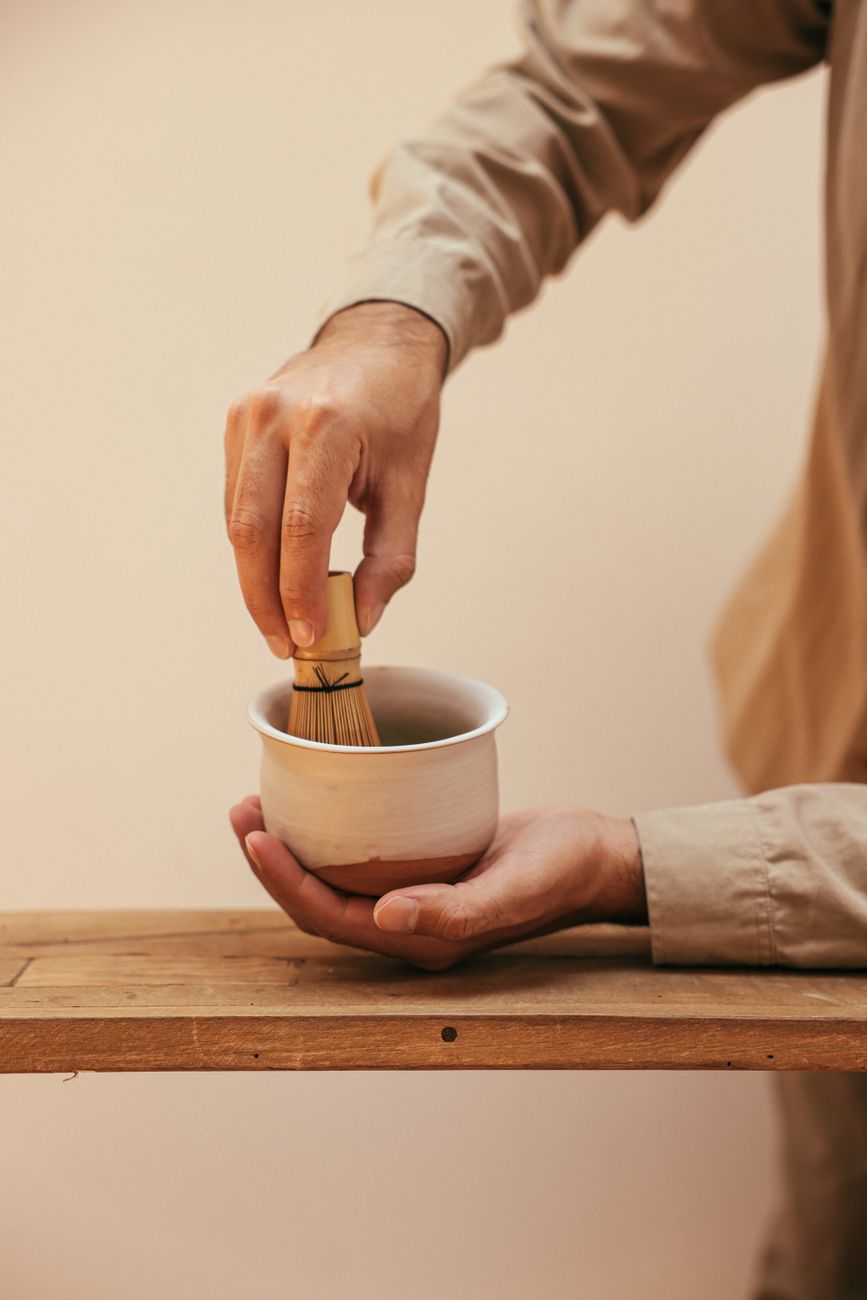 Traditional Japanese chawan tea bowl with frothy green matcha, bamboo whisk resting beside it on wooden surface.