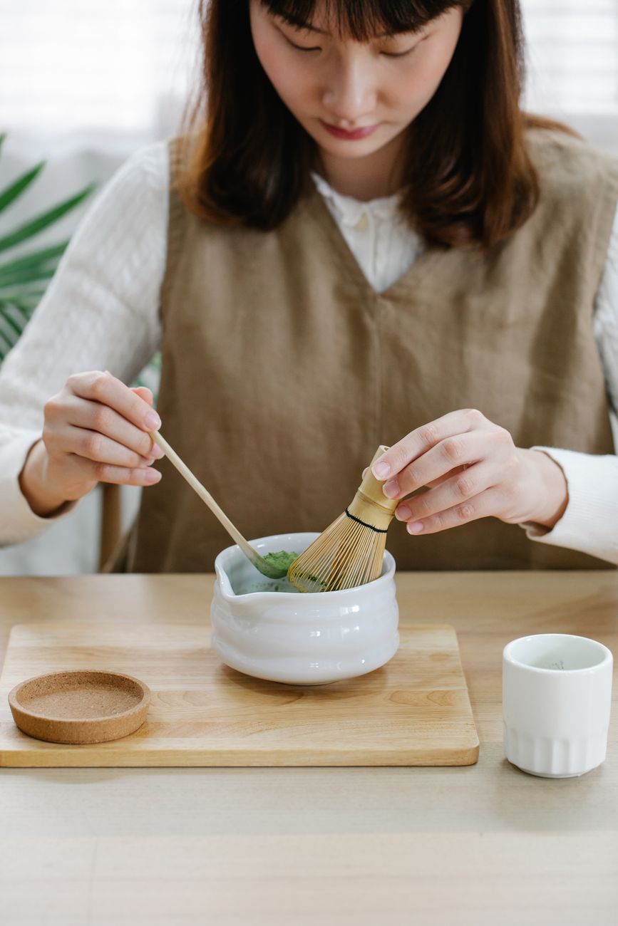 Craftsman's hands carefully shaping a slender bamboo tea scoop over gentle heat to create the traditional curved form.