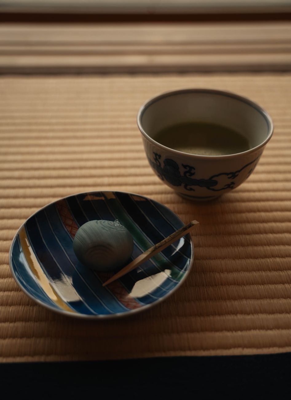 Side-by-side comparison showing bright green matcha powder in a bowl next to loose sencha tea leaves on a bamboo mat.