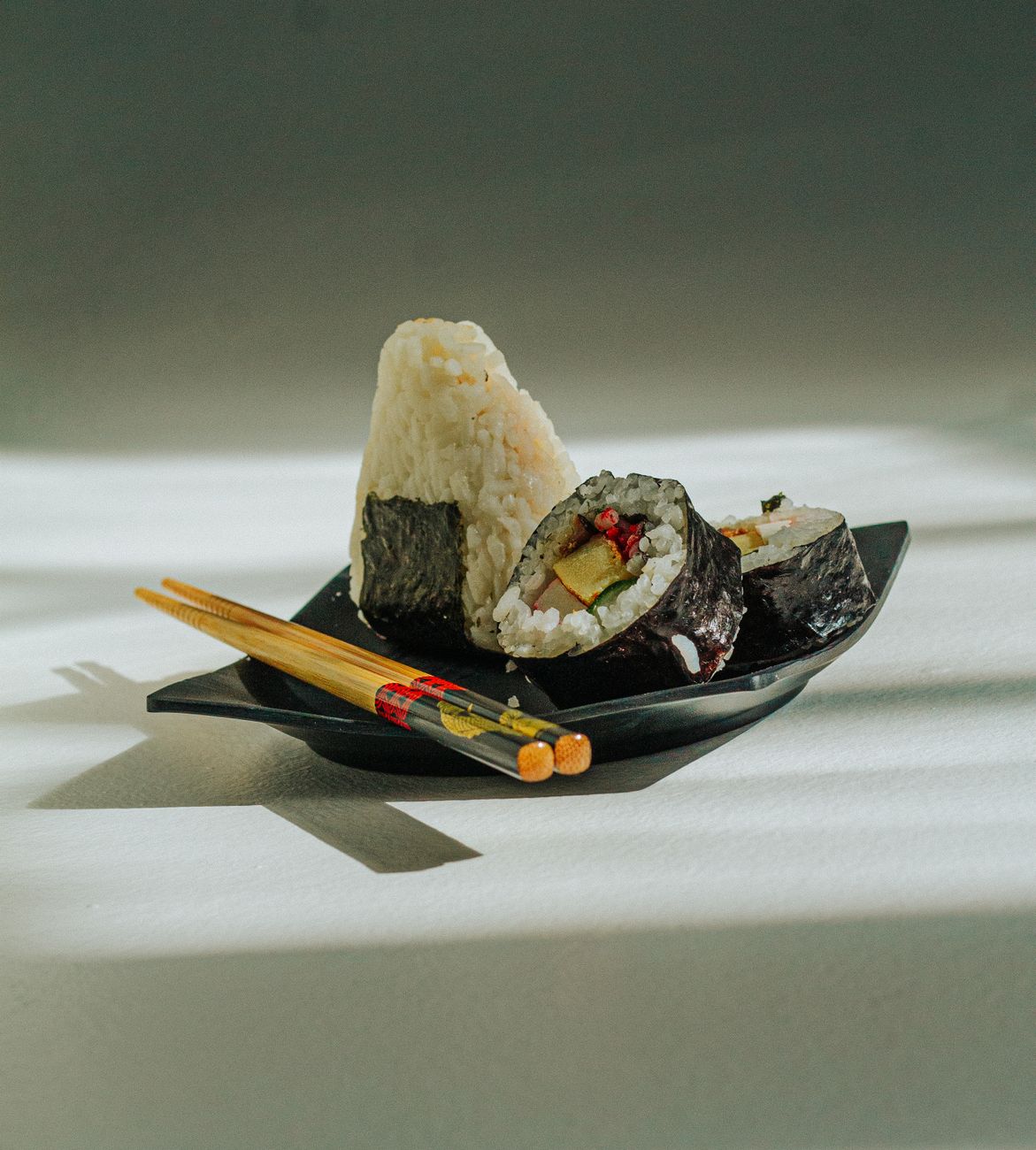 A pair of traditional lacquered Japanese chopsticks with tapered pointed tips resting on a ceramic chopstick rest beside a bowl.
