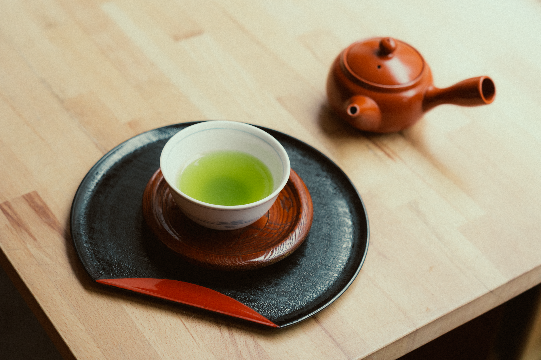 A bamboo whisk whisking thin, bright green usucha matcha in a ceramic tea bowl, creating a frothy layer on the surface.