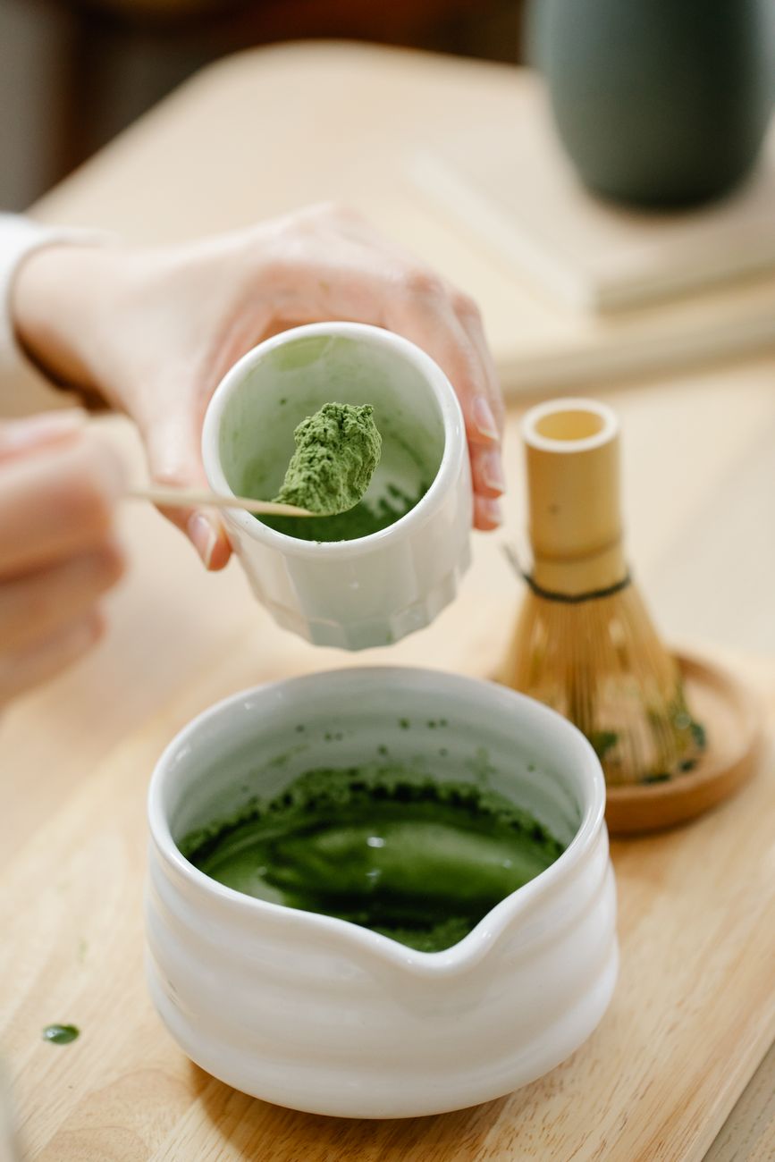 Sealed matcha tin with bamboo scoop resting beside it on a dark wooden surface in soft natural light.