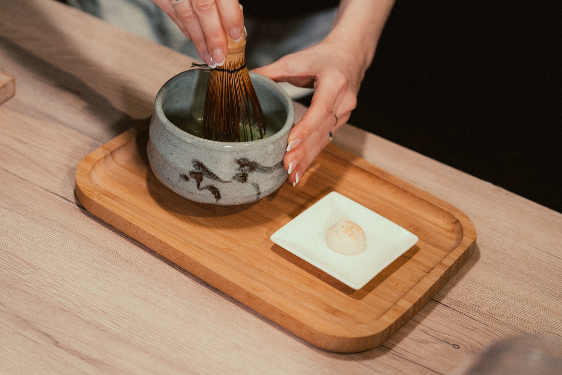 Fine mesh strainer positioned above a ceramic bowl, filtering bright green matcha powder to remove clumps before whisking.