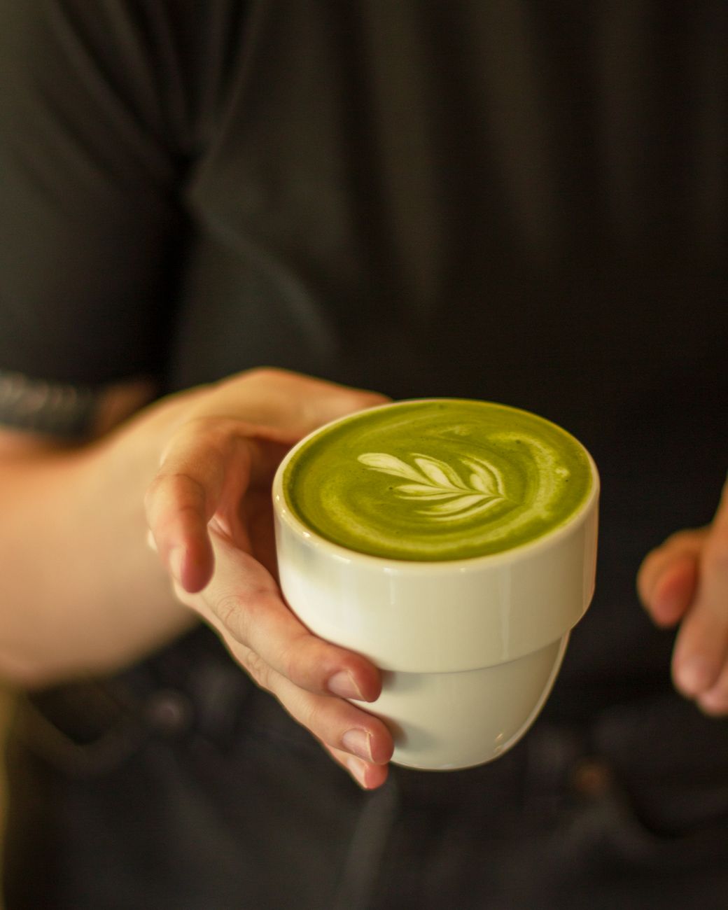Thick, creamy matcha foam with fine bubbles sits atop bright green tea in a traditional ceramic bowl.