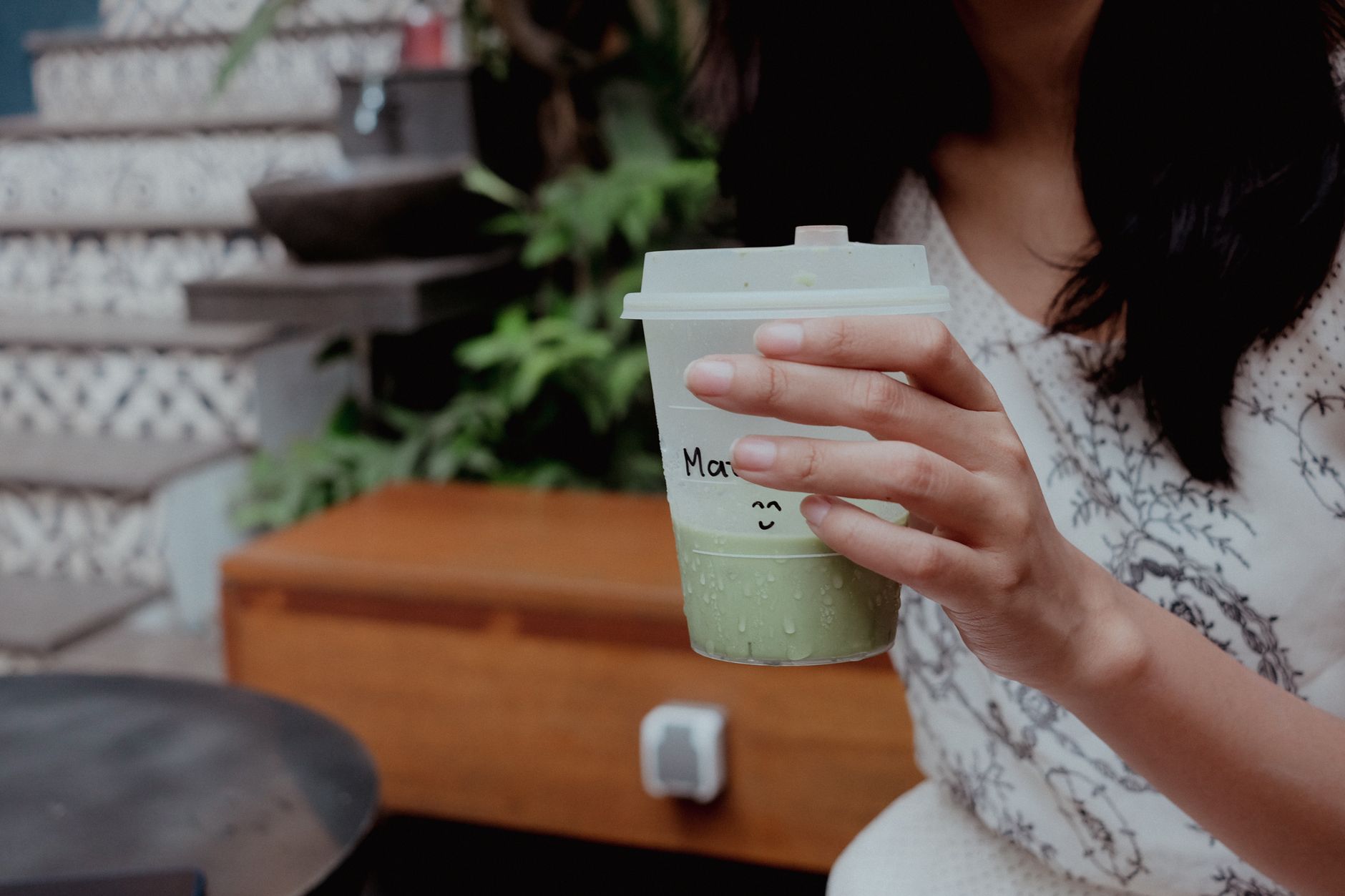 Traditional bamboo whisk whisking vibrant green matcha powder in ceramic bowl beside cup of dark roasted coffee beans