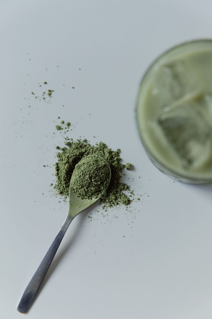 Traditional bamboo whisk whisking vibrant green matcha powder in ceramic bowl beside cup of dark roasted coffee beans
