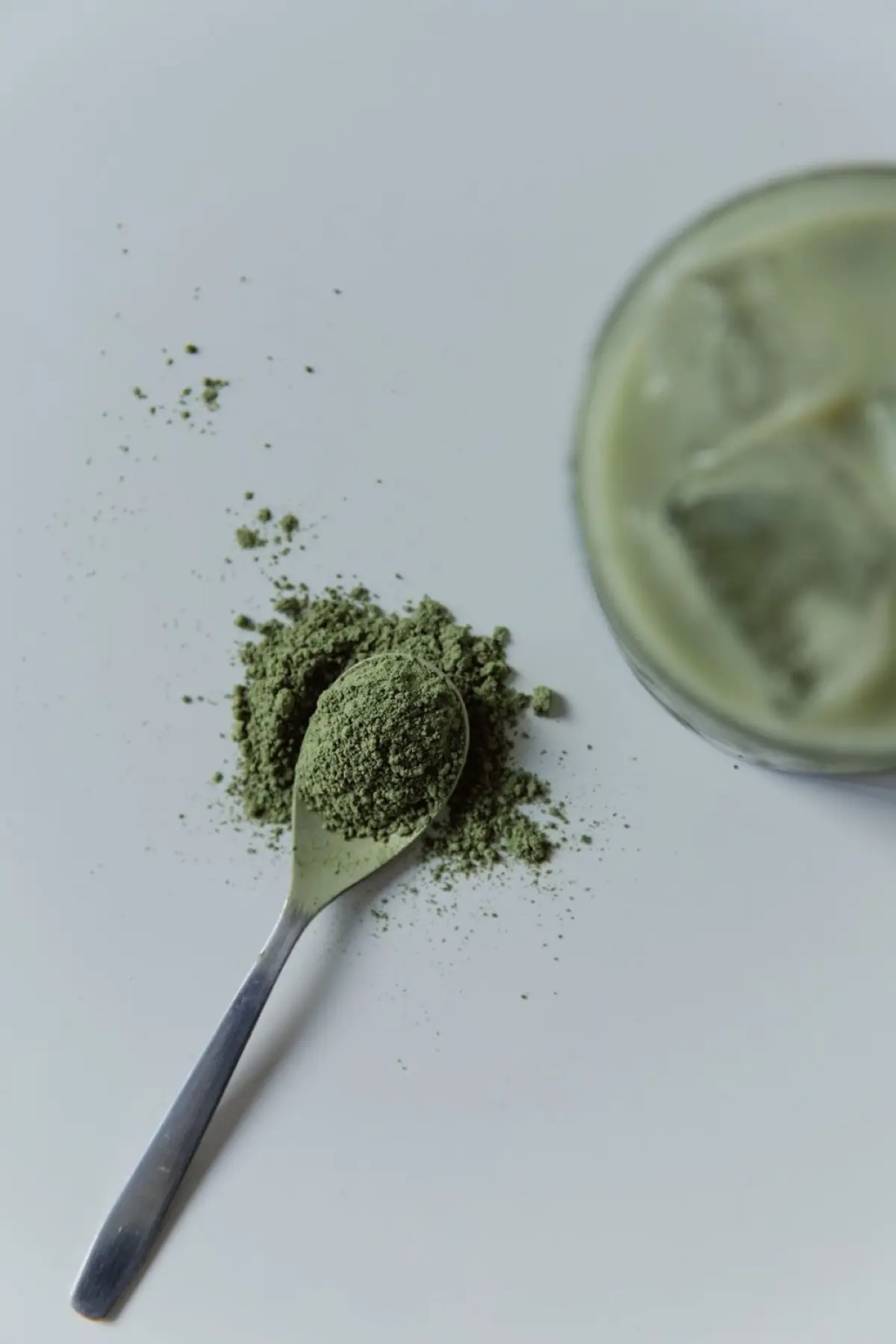 Traditional bamboo whisk whisking vibrant green matcha powder in ceramic bowl beside cup of dark roasted coffee beans