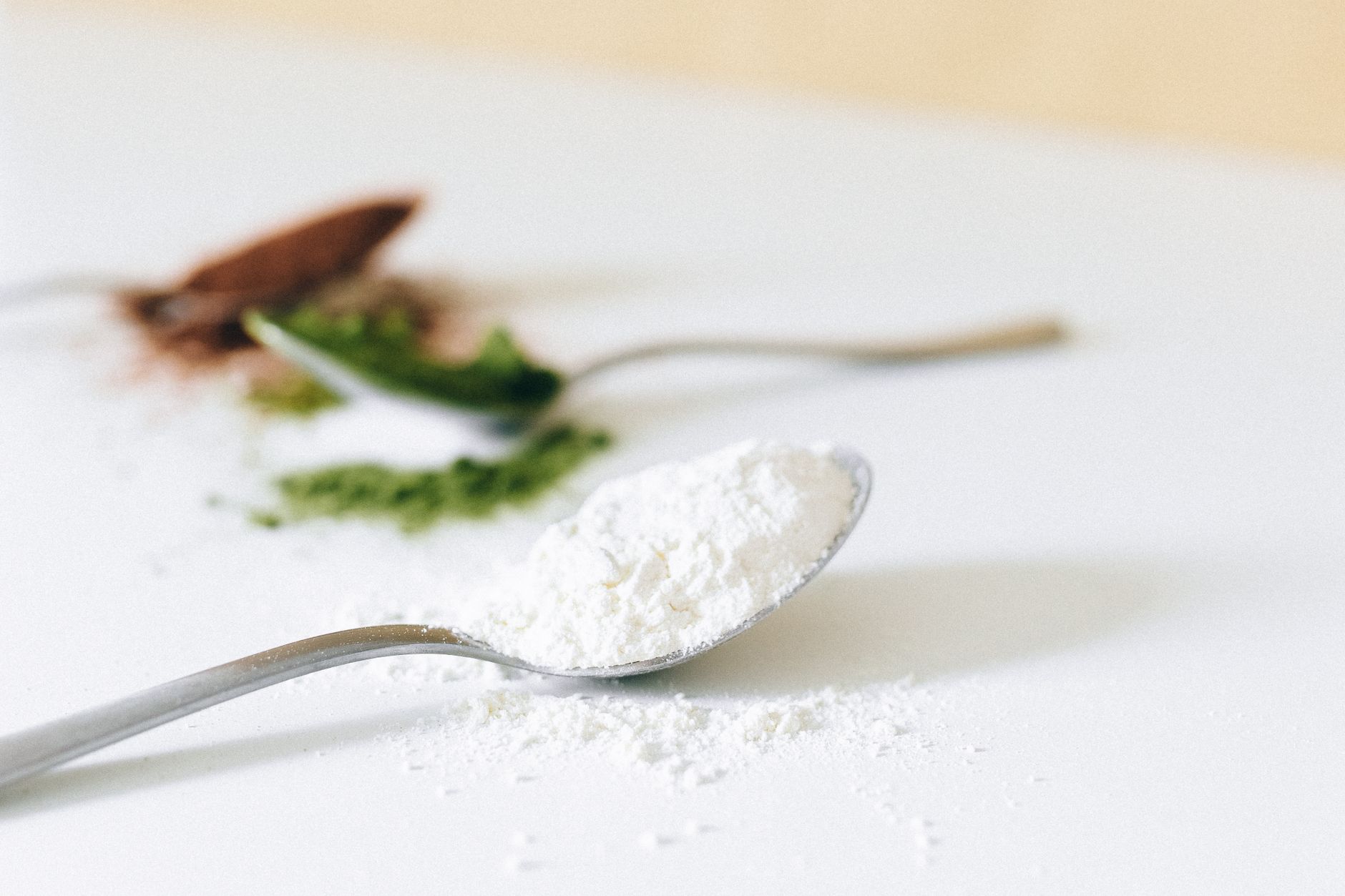 Vibrant green matcha powder in a ceramic bowl beside a bamboo whisk on a wooden table with soft natural light.