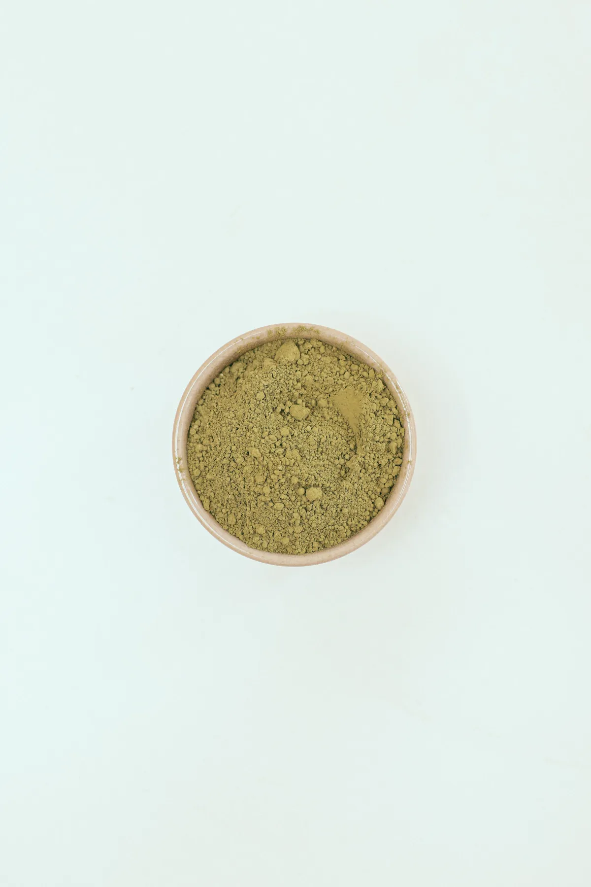 Vibrant green matcha powder in a ceramic bowl beside a bamboo whisk on a wooden table with soft natural light.