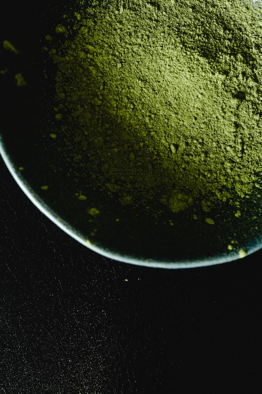 Vibrant green matcha powder in a ceramic bowl beside a bamboo whisk on a wooden table with soft natural light.