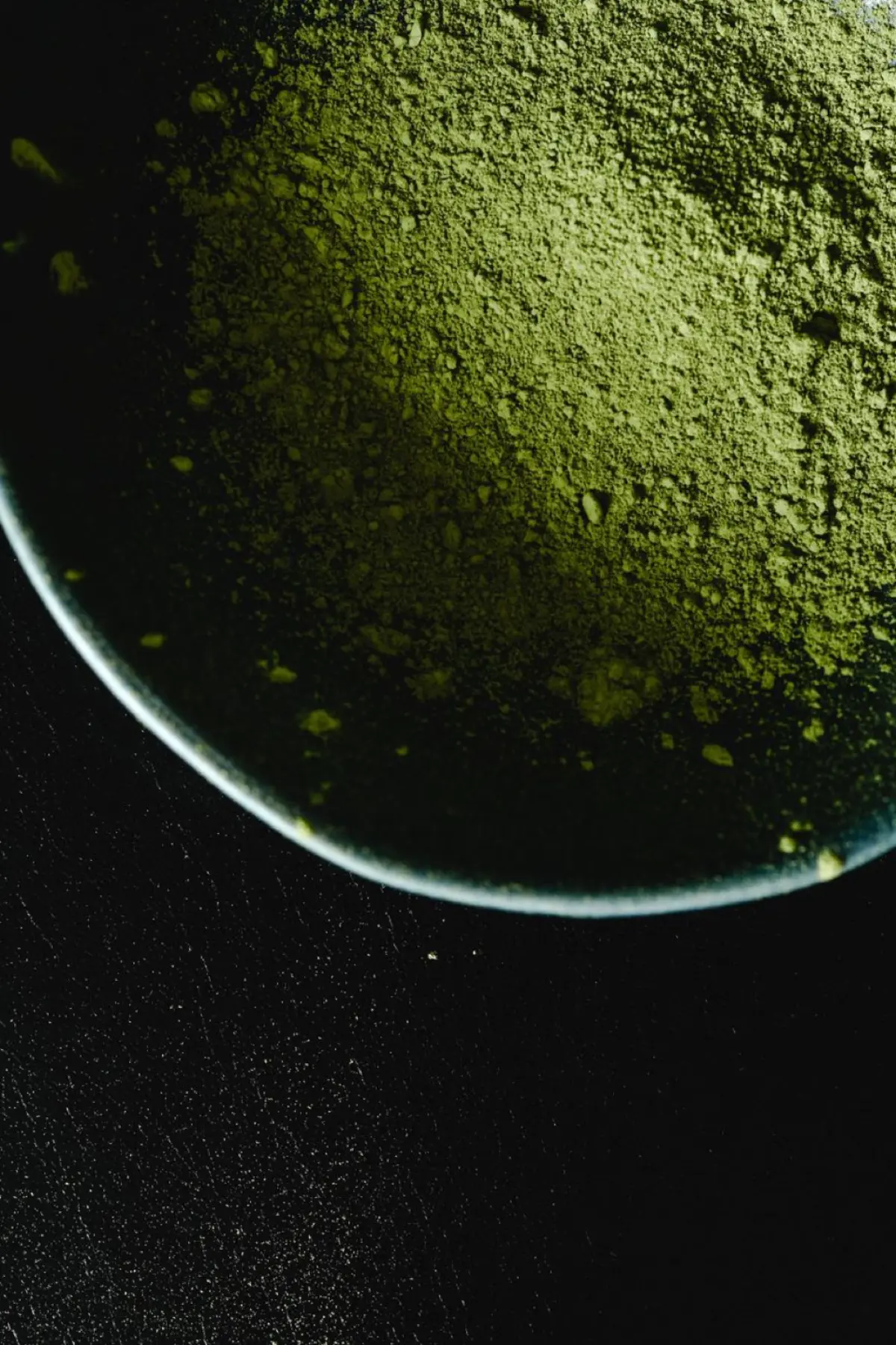 Vibrant green matcha powder in a ceramic bowl beside a bamboo whisk on a wooden table with soft natural light.