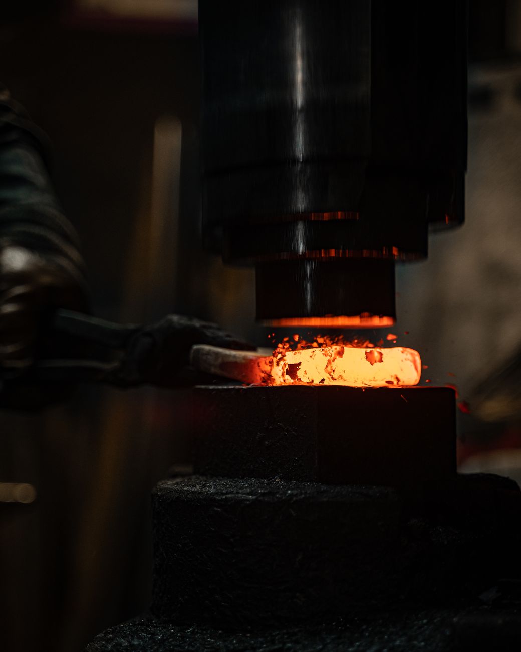 Swordsmith hammering glowing steel on an anvil in a traditional Japanese forge with sparks flying.