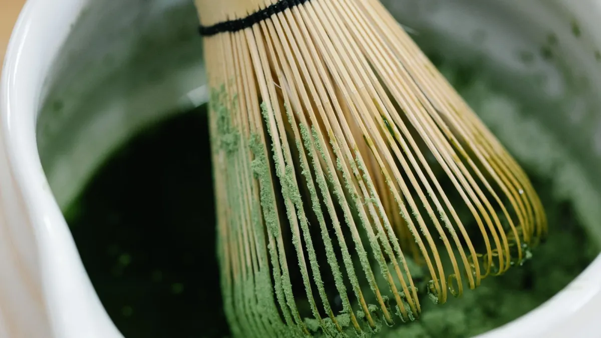 Craftsman's hands splitting a single bamboo node into fine tines using a small knife on a wooden workbench.