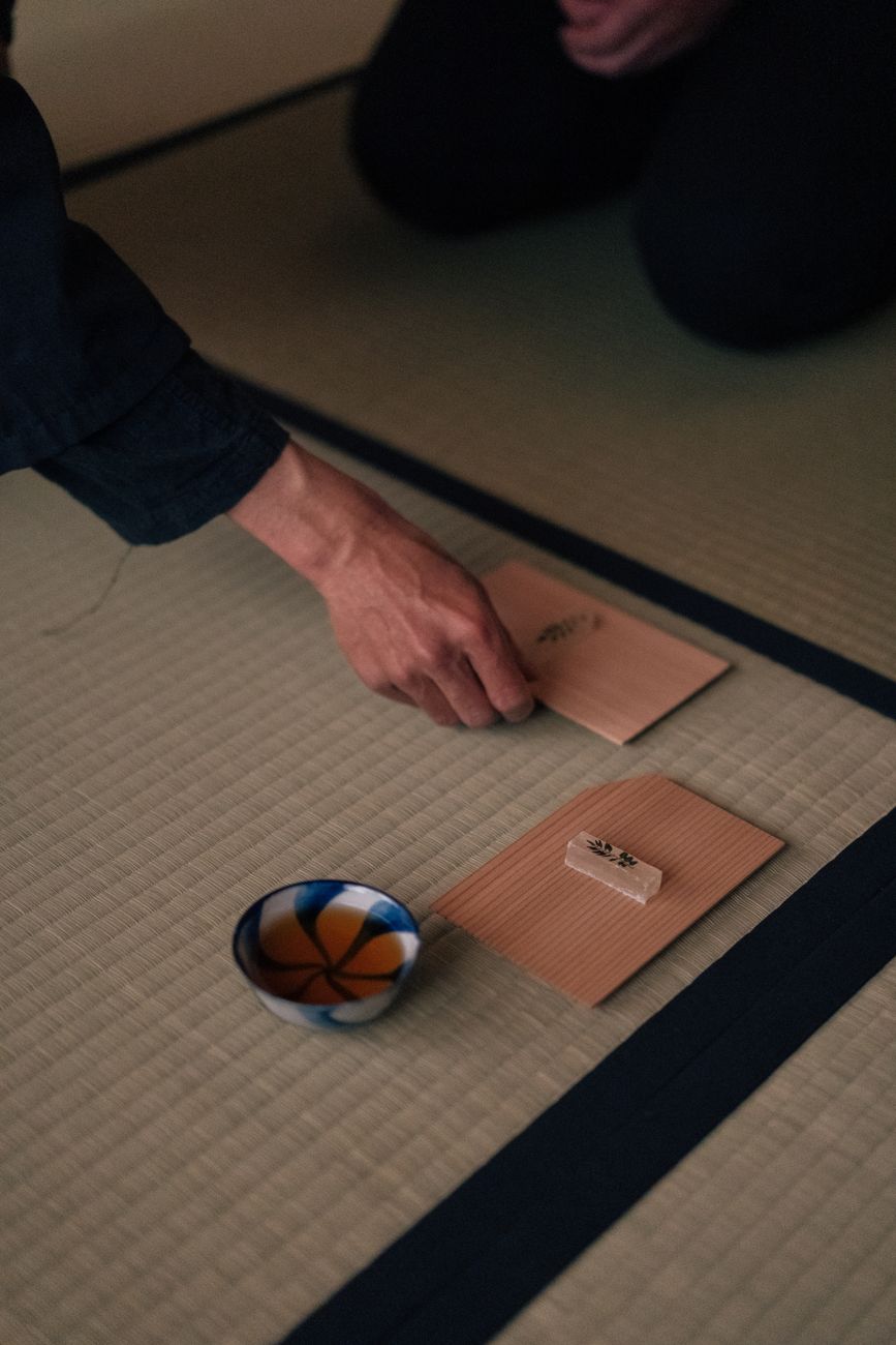 Traditional Japanese tea room with tatami mats, sliding shoji screens, and a simple tokonoma alcove displaying minimalist flower arrangement.