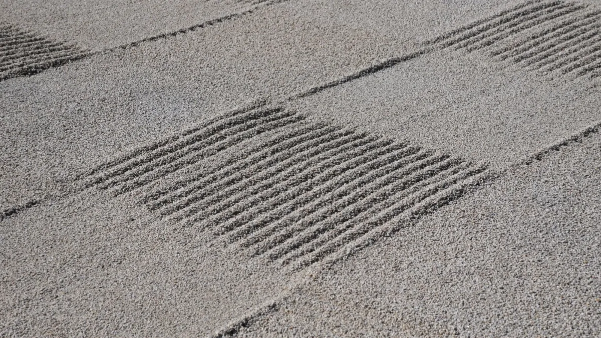 A Japanese karesansui zen garden with raked gravel patterns around carefully placed moss-edged rocks