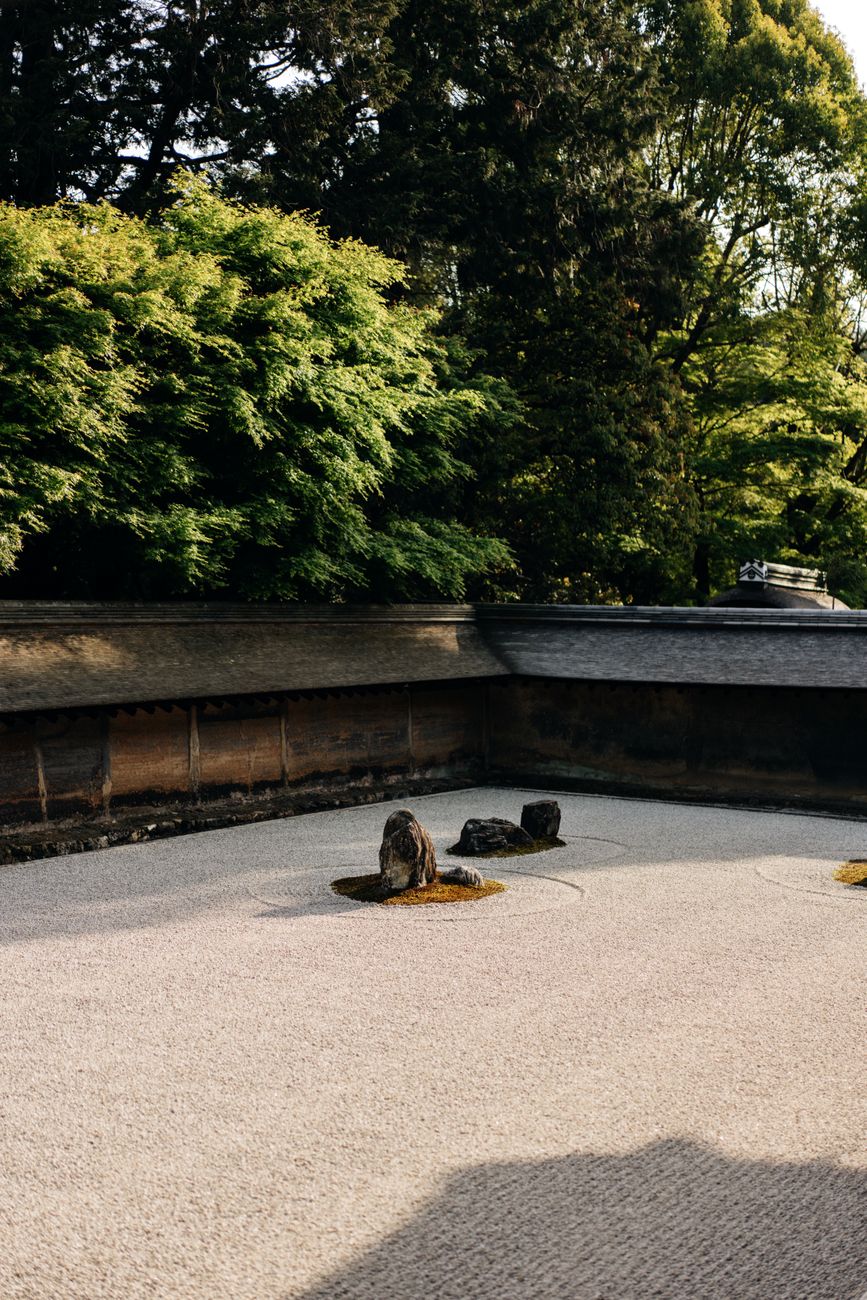 Carefully raked white gravel creates rippling wave patterns around moss-covered rocks in a traditional Japanese temple garden.
